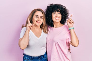 Orta Doğulu anne ve kız, günlük kıyafetler giyip yüzünde kocaman bir gülümsemeyle kameraya el ile işaret ediyorlar.. 