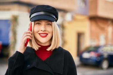 Genç sarışın kadın gülümsüyor. Şehirdeki akıllı telefondan konuşuyor..