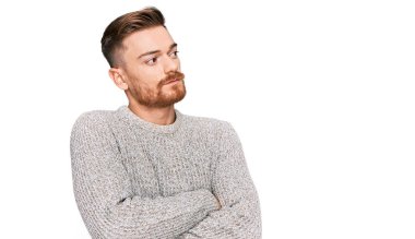 Genç kızıl saçlı, sıradan bir kazak giymiş kolları çaprazlanmış ve kendinden emin bir şekilde yan tarafa bakıyor. 