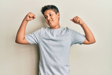 Gündelik gri tişört giyen genç İspanyol çocuk gururla gülümseyen kol kaslarını gösteriyor. fitness konsepti. 