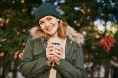 Beyaz kız gülümsüyor. Parkta kahve içiyor.