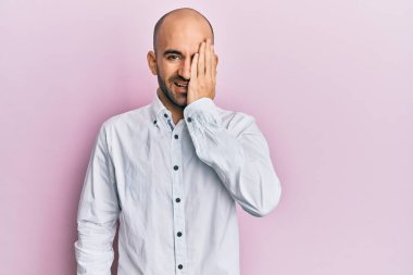 Latin asıllı genç adam gündelik giysiler giyiyor. Bir gözünü eliyle kapatıyor. Yüzünde kendine güvenen bir gülümseme ve sürpriz bir duygu var.. 