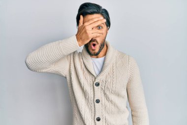 Gündelik kıyafetler giyen genç İspanyol adam şok içinde yüzünü ve gözlerini eliyle kapatıyor, parmaklarından korkuyla bakıyor. 