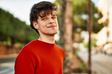 Genç İspanyol adam gülümseyerek şehirde mutlu mesut dikiliyor.