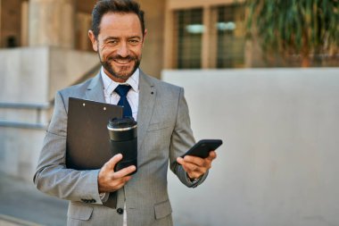 Orta yaşlı işadamı akıllı telefon kullanıyor ve şehirde kahve içiyor..