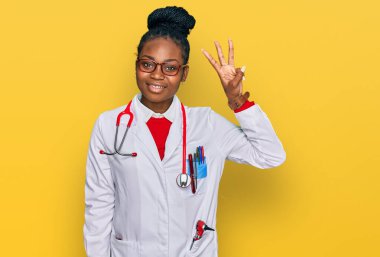 Genç Afro-Amerikan kadın doktor üniforması ve steteskop giyiyor. Üç numarayı gösterip işaret ederken kendinden emin ve mutlu bir şekilde gülümsüyor.. 