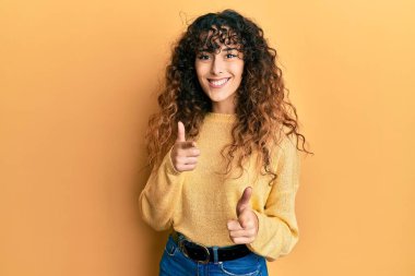 Günlük kıyafetler giyen genç İspanyol kız mutlu ve komik yüzüyle kamerayı işaret ediyor. iyi enerji ve titreşimler. 