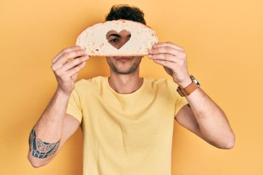 Gözünün üzerinde kalp şeklinde ekmek tutan genç İspanyol adam öpüşürken kameraya bakıyor. aşk ifadesi. 