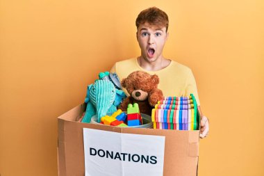 Kafkasyalı genç adam oyuncaklarla dolu bir bağış kutusu tutuyor. Şaşırmış ve şaşırmış bir ifade, korku ve heyecanlı bir yüz ifadesi var.. 