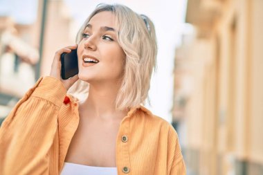 Genç sarışın kız gülümsüyor. Şehirdeki akıllı telefondan konuşuyor..