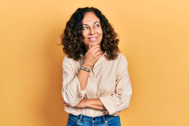 Orta yaşlı İspanyol kadın. Elleri çenesinde gündelik giysiler giyip soru soruyor. Düşünceli bir ifade. Düşünceli bir yüzle gülümsüyor. şüphe kavramı. 