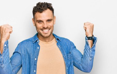 Gündelik kıyafetler giyen genç İspanyol adam gururla bağırıyor, zaferi ve başarıyı kutluyor. Kollarını kaldırarak heyecanla bekliyor. 