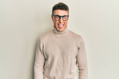 Balıkçı yaka kazak giyen İspanyol genç adam komik bir ifadeyle dilini dışarı çıkartıyor. duygu kavramı. 