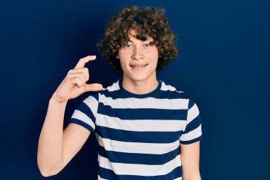 Yakışıklı, çizgili tişört giyen, gülümseyen, kendine güvenen, el hareketi yapan, parmaklarıyla işaret yapan ve kameraya bakan genç bir adam. ölçüm kavramı. 