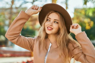 Genç sarışın kız gülümsüyor, mutlu bir şekilde şehirde duruyor..