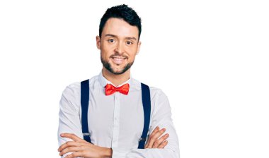 Sakallı, hippi görünümlü, papyonlu, pantolon askısı takan, kollarını kavuşturup kameraya gülümseyen İspanyol bir adam. pozitif kişi. 