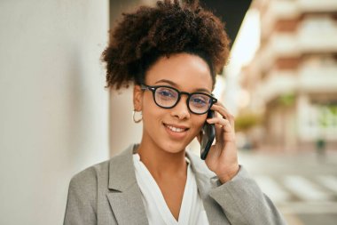 Genç afro-amerikan iş kadını gülümseyerek şehirdeki akıllı telefondan konuşuyor..