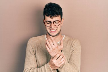 Günlük kıyafetler giyen ve gözlük takan genç İspanyol adam ellerinde ve parmaklarında ağrı, iltihaplanma 