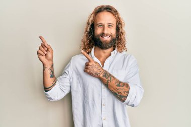 Sakallı, uzun saçlı, sıradan beyaz gömlekli, gülümseyen ve kameraya bakan yakışıklı bir adam.. 