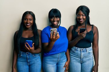 Üç Afro-Amerikalı arkadaş mutlu ve havalı bir gülümsemeyle akıllı telefon kullanıyor. şanslı kişi. 