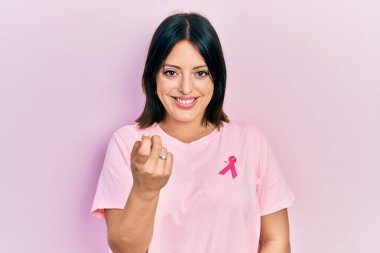 Tişörtüne pembe kanser kurdelesi takmış genç İspanyol kadın seni çağırıyor. Gel buraya. Mutlu bir şekilde karşıla ve gülümse. 