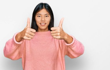 Güzel, genç Asyalı bir kadın günlük kışlık süveter giyiyor. Elleriyle olumlu bir jest yapıyor. Gülümsüyor ve başarı için seviniyor. kazanan jest. 