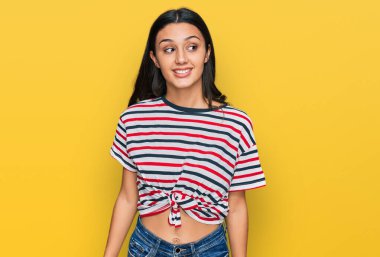 Günlük kıyafetler giyen genç İspanyol kız yüzünde gülümsemeyle yan yana bakıyor, doğal bir ifade. Kendinden emin gülen. 