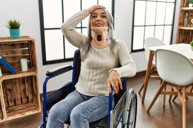 Orta yaşlı, gri saçlı, tekerlekli sandalyede oturan, tasmalı bir kadın. Stresli ve hayal kırıklığına uğramış, şaşırmış ve kızgın bir yüzü var. 