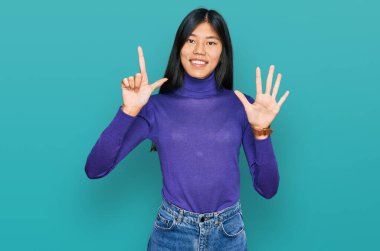 Güzel, genç Asyalı bir kadın günlük kıyafetler giyer ve yedi numaralı parmaklarını göstererek gülümseyerek mutlu ve kendinden emin bir şekilde gösterir.. 