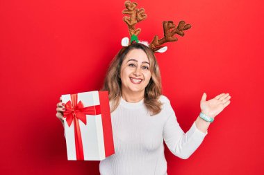 Orta yaşlı, beyaz, şirin Noel geyiği boynuzları takan bir kadın. Elleri havada bir gülümsemeyle zaferi kutluyor. 