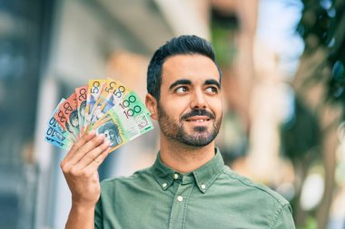 Genç İspanyol gülümseyen adam Avustralya dolarlarını şehirde tutarken mutlu..