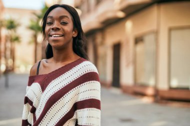 Genç Afrikalı Amerikalı kadın gülümseyerek şehirde mutlu mesut duruyor..