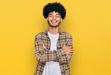 Afro saçlı, sıradan kıyafetler giyen, kollarını kavuşturup kameraya gülümseyen Afro-Amerikan genç adam. pozitif kişi. 