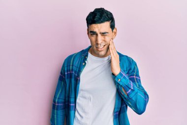 Yakışıklı, günlük kıyafetler giyen, diş ağrısı ya da diş hastalığından dolayı ağızlarına acı dolu bir ifadeyle dokunan yakışıklı bir İspanyol. dişçi 