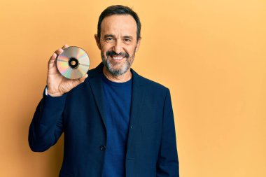 Orta yaşlı İspanyol bir adam diski tutuyor. Pozitif ve mutlu görünüyor. Kendine güvenen bir gülümsemeyle dişlerini gösteriyor. 