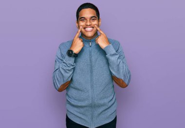 Genç, yakışıklı, sıradan bir kazak giyen, ağzı açık gülümseyen, parmakları işaret eden ve zorla gülümseyen bir İspanyol. 