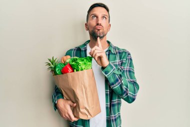 Sakallı yakışıklı bir adam, elinde poşetle bakkaldan aldıklarını alıp parmak çenesinde şüpheyi düşünüp kafasını kaldırıyor. 