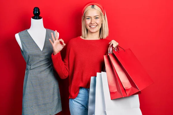 美しいブロンドの女性は指でOkサインを行うショッピングバッグを保持し フレンドリーなジェスチャー優れたシンボル — ストック写真