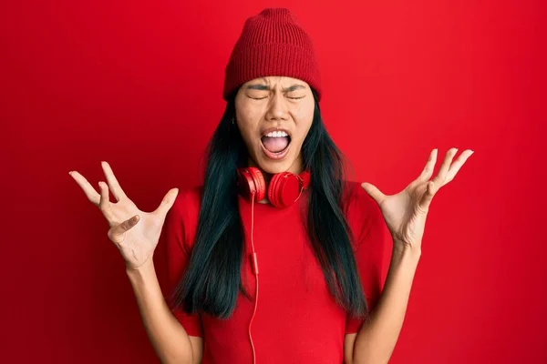 年轻的中国妇女一边用耳机听音乐 一边疯狂地喊叫着 带着咄咄逼人的表情和胳膊大喊大叫 沮丧的概念 — 图库照片