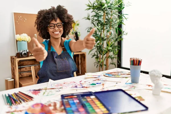 美丽的非洲裔美国女人 在艺术工作室里画着非洲的头发 她赞成用手做积极的手势 微笑着竖起大拇指 为成功感到高兴 优胜手势 — 图库照片