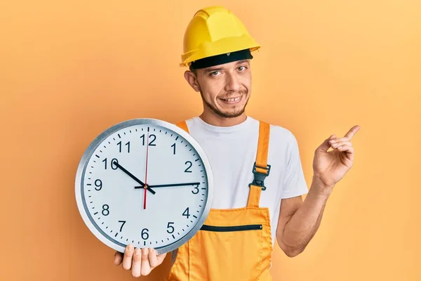 Joven Hispano Vistiendo Uniforme Constructor Reloj Mano Dura Sonriendo Feliz —  Fotos de Stock