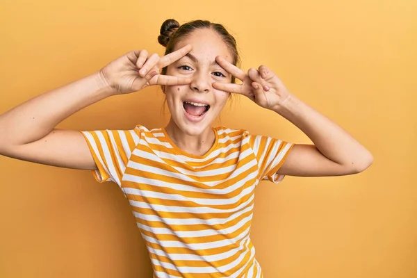 美しいブルネットの女の子は顔の上に指で平和のシンボルを行うカジュアルな縞模様のTシャツを着て 陽気に示す勝利を笑顔 — ストック写真