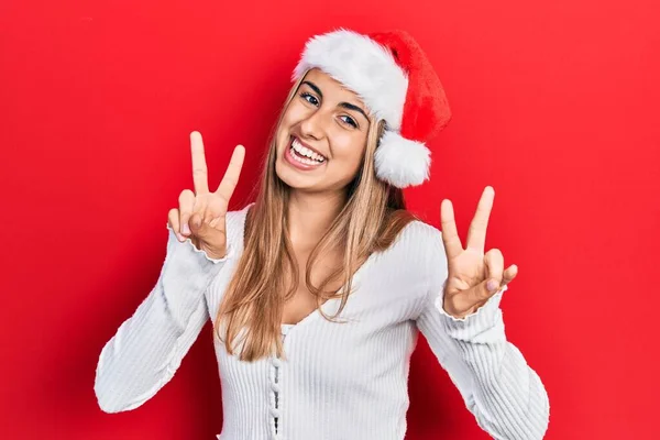 Красивая Латиноамериканка Рождественской Шляпе Улыбающаяся Камеру Показывающая Пальцы Делающие Знак — стоковое фото