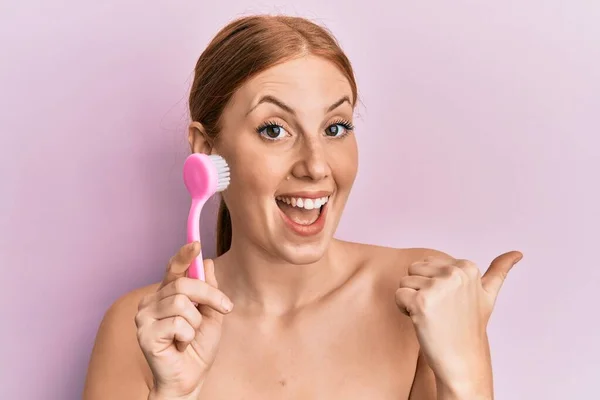 Young Irish Woman Using Facial Exfoliating Brush Pointing Thumb Side — Stock Photo, Image