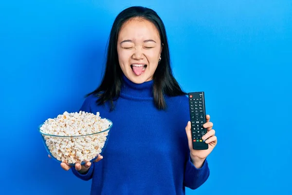 若いです中国の女の子食べるポップコーン使用してテレビコントロールステッキング舌アウト幸せなですとともに面白い式 — ストック写真