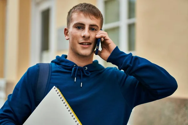 年轻的金发学生拿着笔记本在大学里用智能手机聊天 — 图库照片