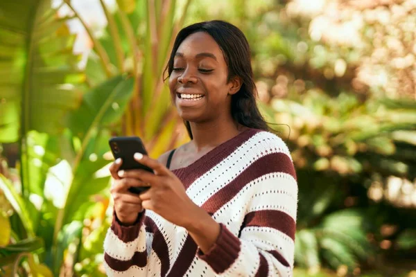 若いアフリカ系アメリカ人の女性が公園でスマートフォンを使って笑顔で幸せ — ストック写真