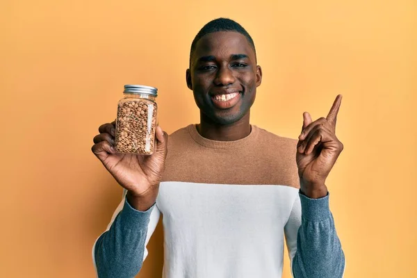 Joven Hombre Afroamericano Sosteniendo Tarro Lentejas Sonriendo Feliz Señalando Con — Foto de Stock