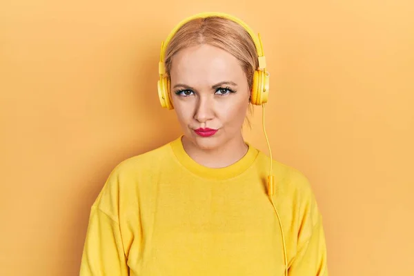 若いブロンドの女性は 問題のために動揺を眉をひそめて 懐疑的で緊張したヘッドフォンを使用して音楽を聴く 否定的な人 — ストック写真