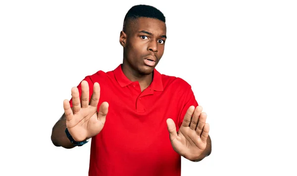 カジュアルな赤いTシャツを着た若いアフリカ系アメリカ人男性は 恐怖と嫌な表情で拒否と否定を示す手のひらを離れて移動します 止めて禁止する — ストック写真
